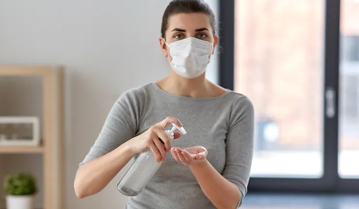 Masked girl applying hand sanitizer from a bottle