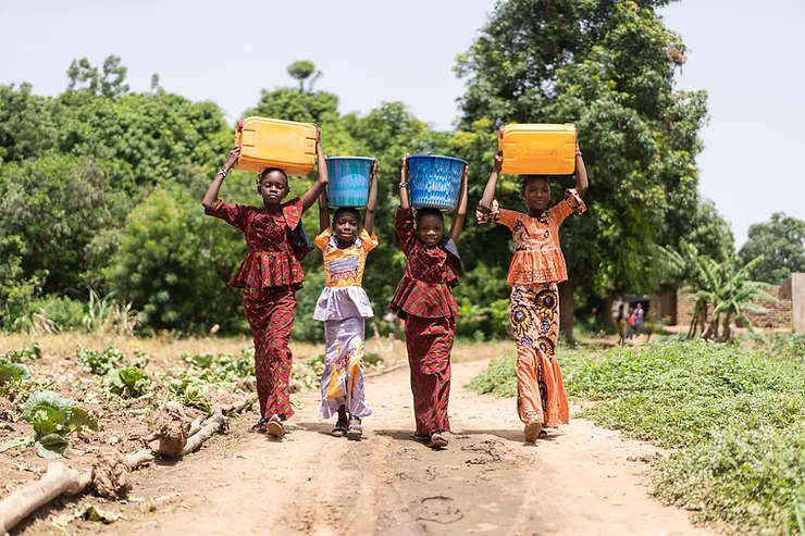 Four young girls walking in a village, carrying water pots on their heads