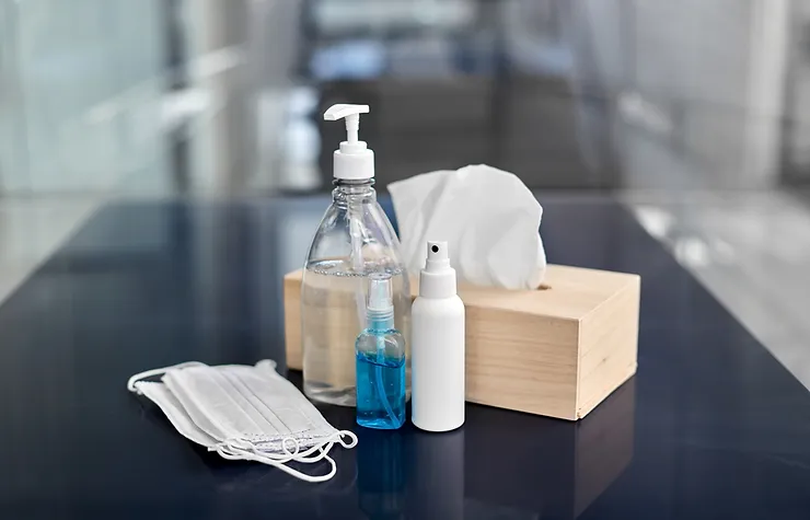 A table with several masks, sanitizer bottles, and a tissue box placed on it