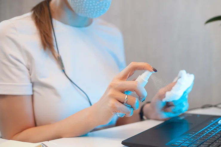 A young woman applying sanitizer spray on a microfiber cloth before cleaning her laptop keyboard