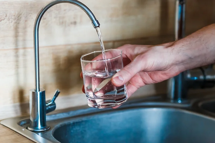 Hand holding a glass under a running tap to fill it with water.