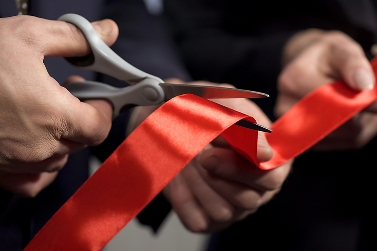 A man using scissors to ceremoniously cut a bright red ribbon, marking an inauguration of distribution center.