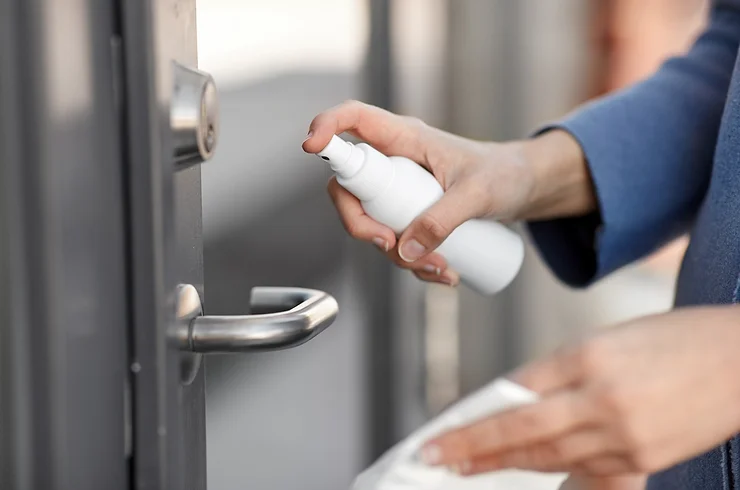 Person sanitizing a door handle with a spray bottle to maintain hygiene