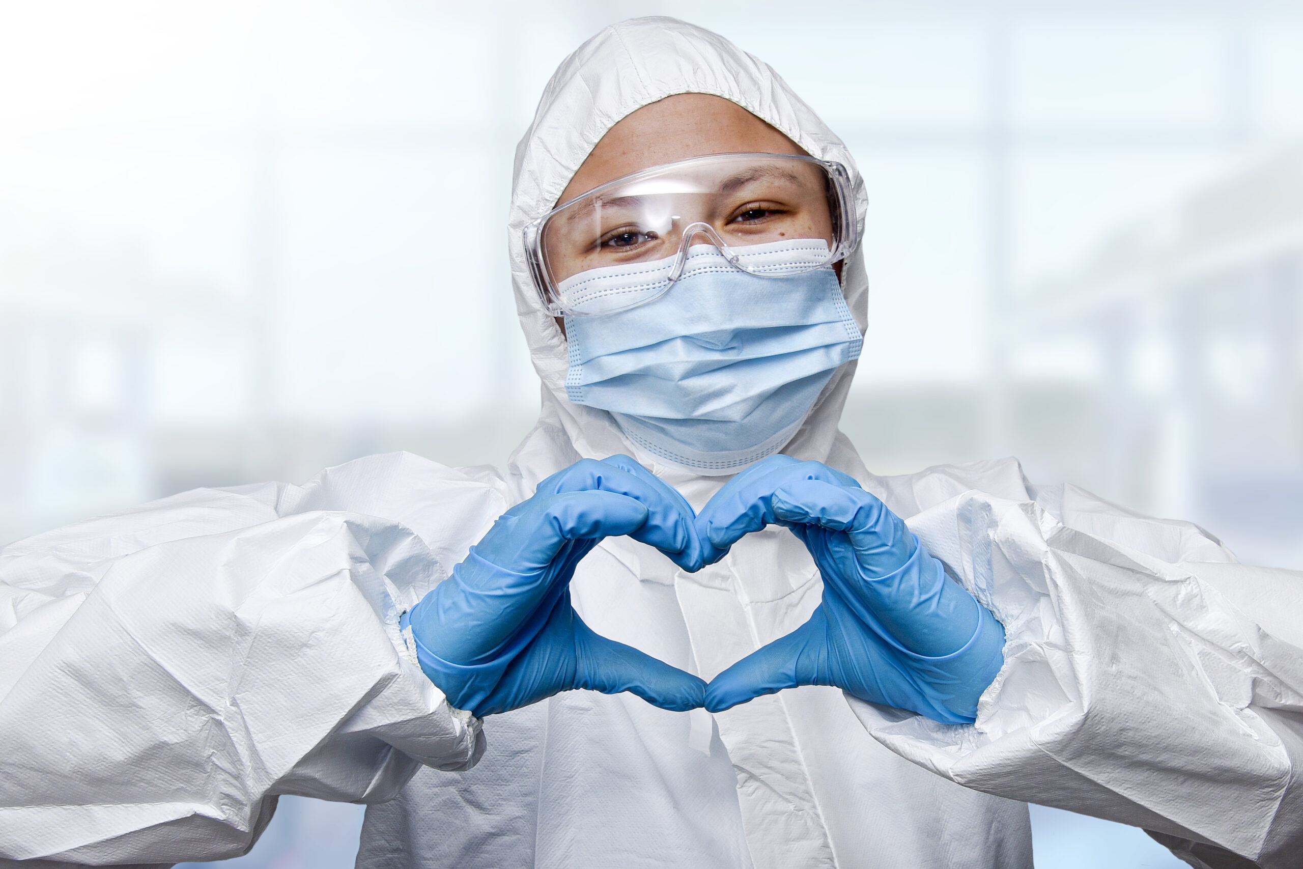 A female pharmacist with protective medical mask and glasses making a heart shape with hands