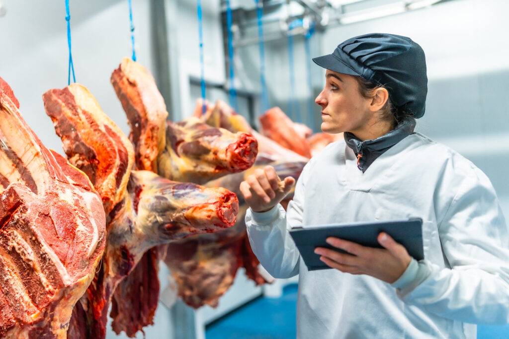 Butcher using technology in a innovative meat processing factory checking the meat using digital tablet